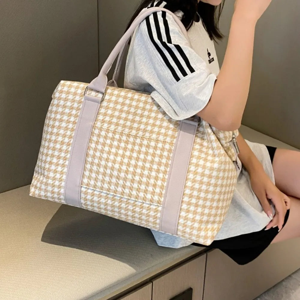 A lady holding a beige and white houndstooth handbag with light gray handles and a structured, rounded shape. Soft and stylish—perfect for everyday fashion.