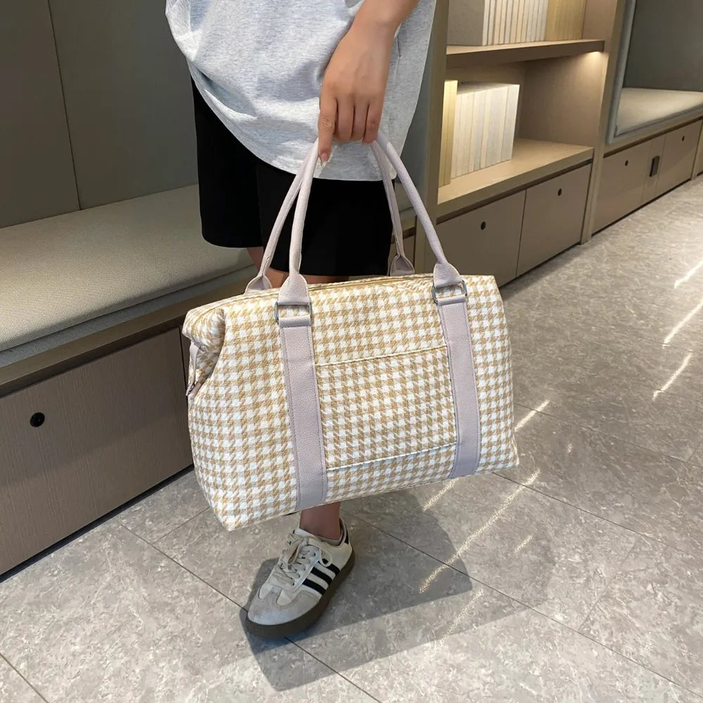 A person posing with a beige and white houndstooth handbag with light gray handles and a structured, rounded shape. Soft and stylish—perfect for everyday fashion.
