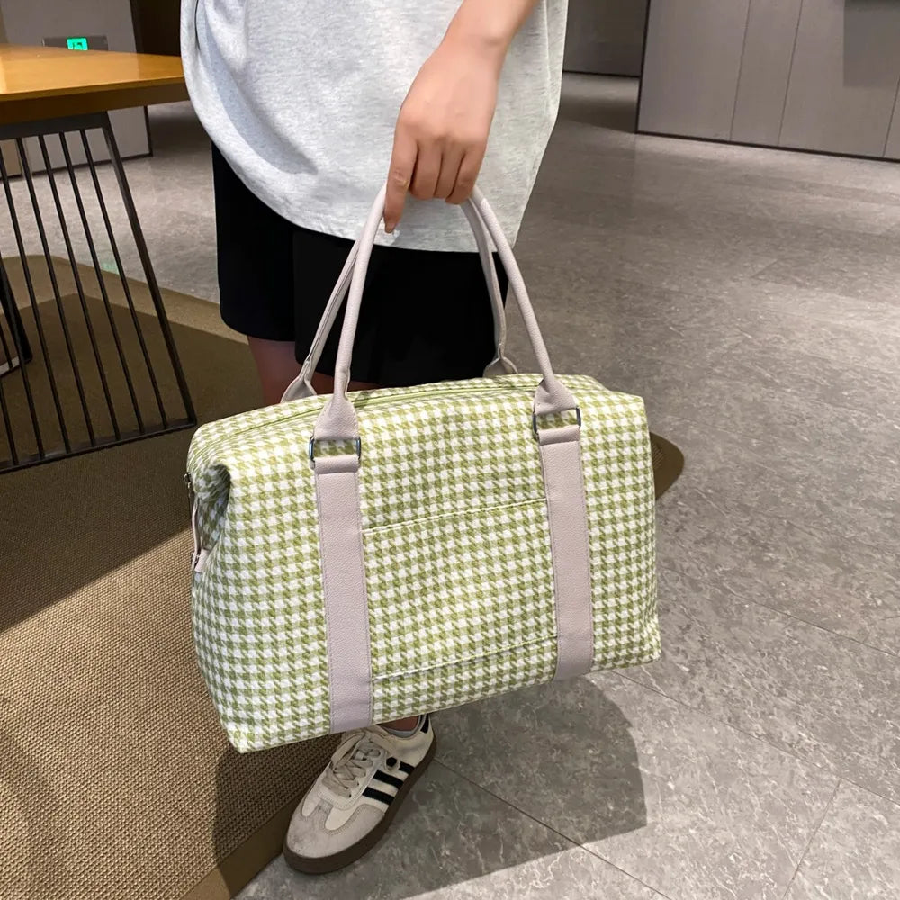 Person holding a green and white houndstooth handbag with light beige handles and trim, placed beside stacked books. Soft, structured, and stylish—ideal for casual or semi-formal use.