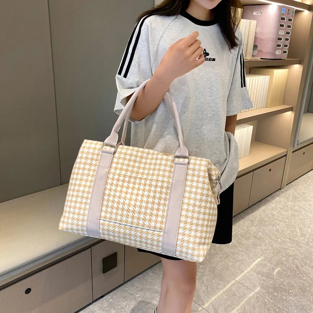 A woman posing with a beige and white houndstooth handbag with light gray handles and a structured, rounded shape. Soft and stylish—perfect for everyday fashion.
