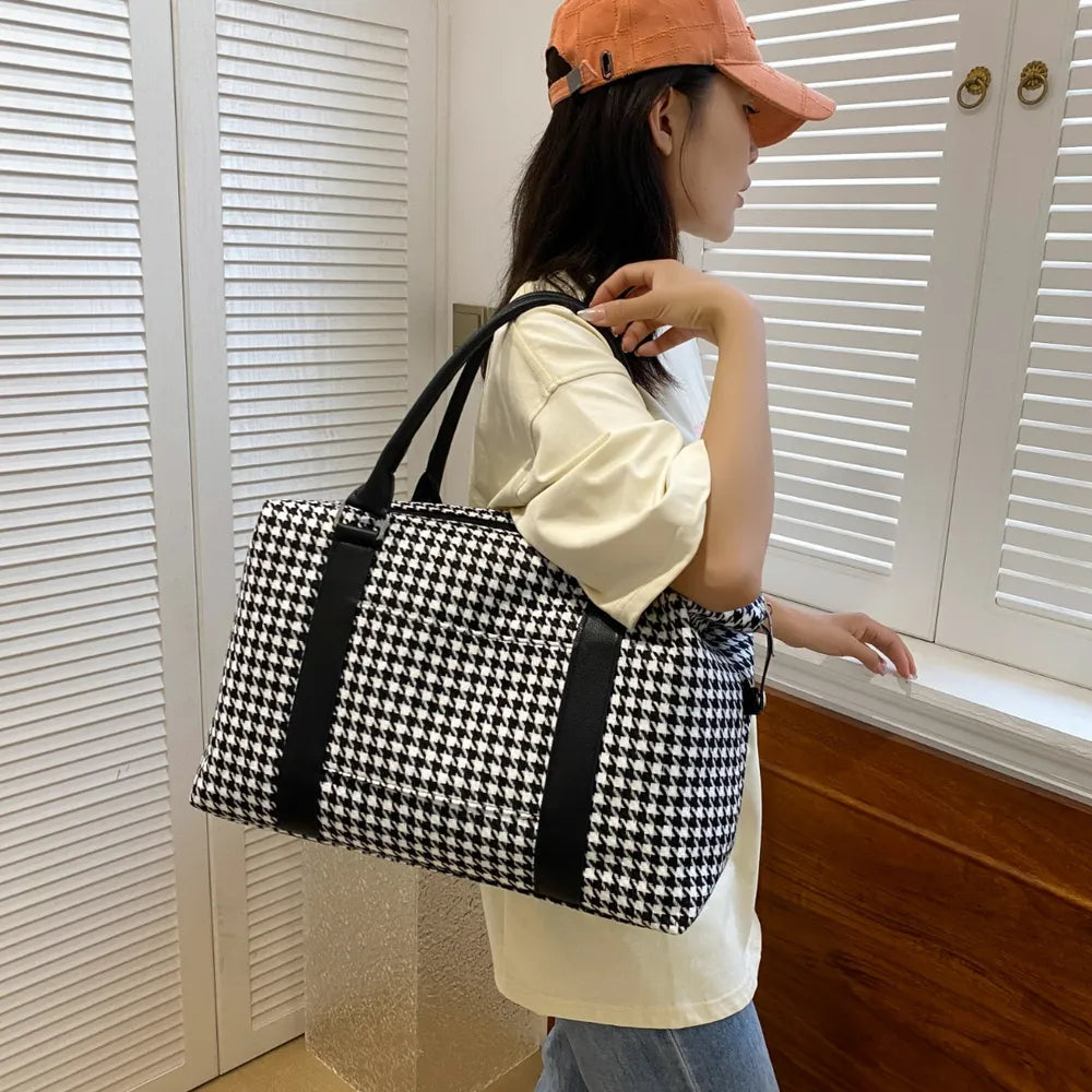 A lady holding a black and white houndstooth handbag with black leather handles and accents, featuring a structured rectangular shape. Chic and modern—perfect for stylish everyday wear.