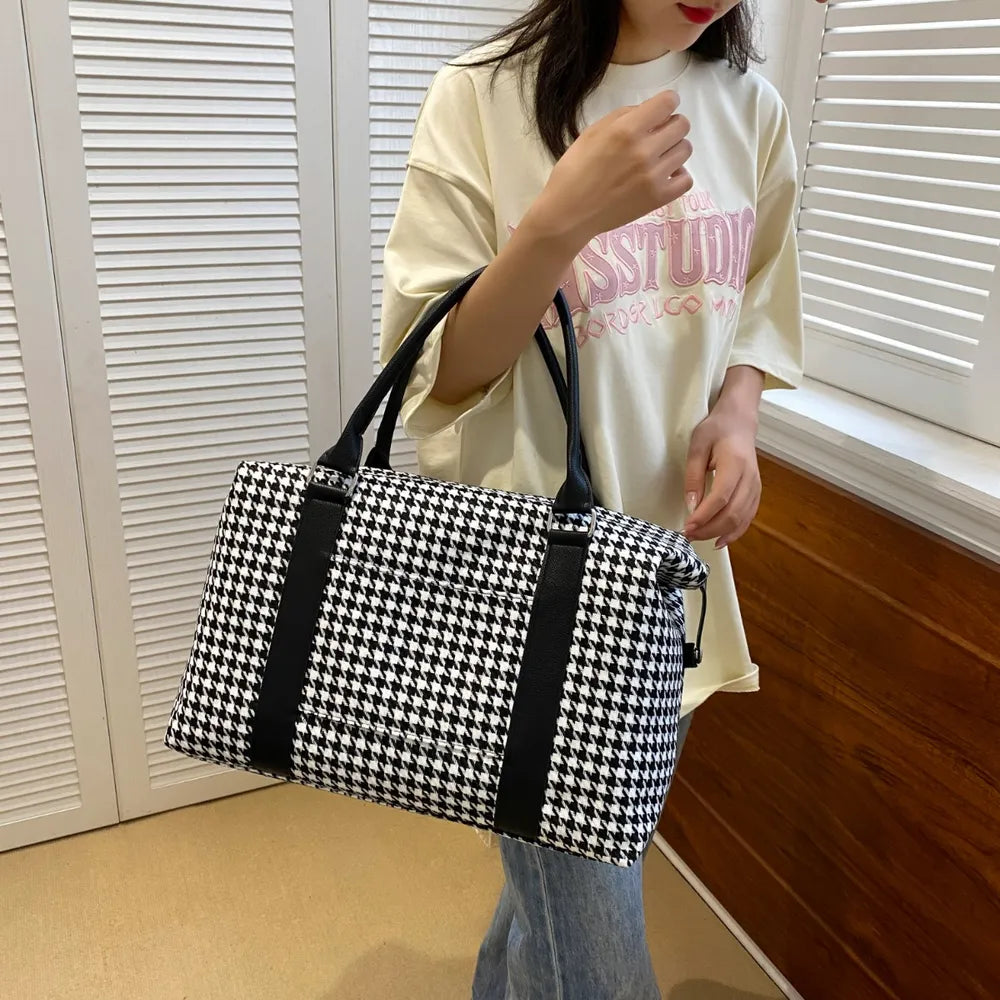 A lady holding a black and white houndstooth handbag with black leather handles and accents, featuring a structured rectangular shape. Chic and modern—perfect for stylish everyday wear.