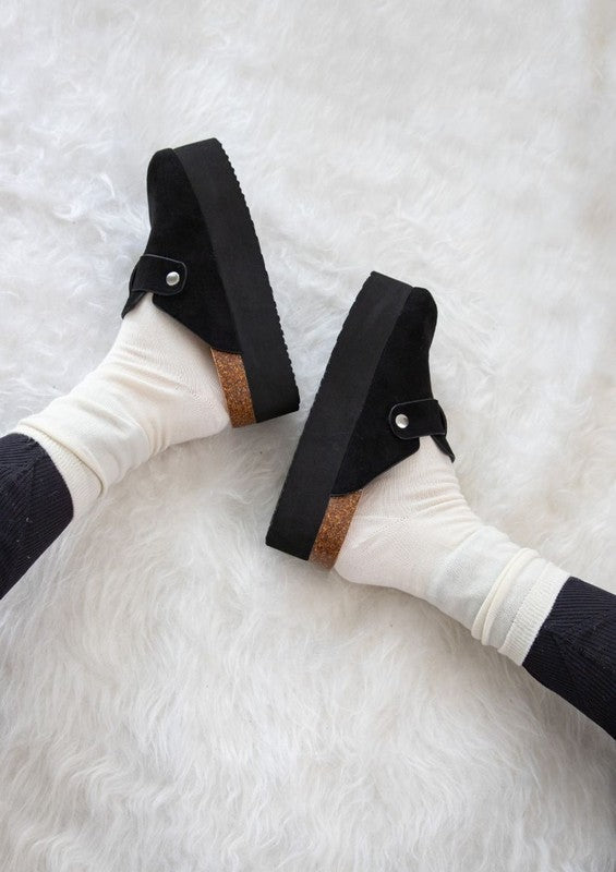 Chunky platform mules featuring adjustable ankle strap with buckle, closed-toe cut, layered flatform sole, slip-on design