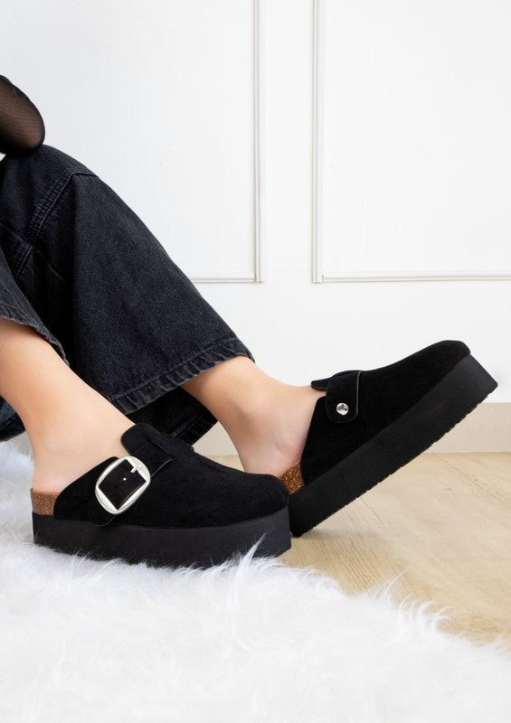 Chunky platform mules featuring adjustable ankle strap with buckle, closed-toe cut, layered flatform sole, slip-on design