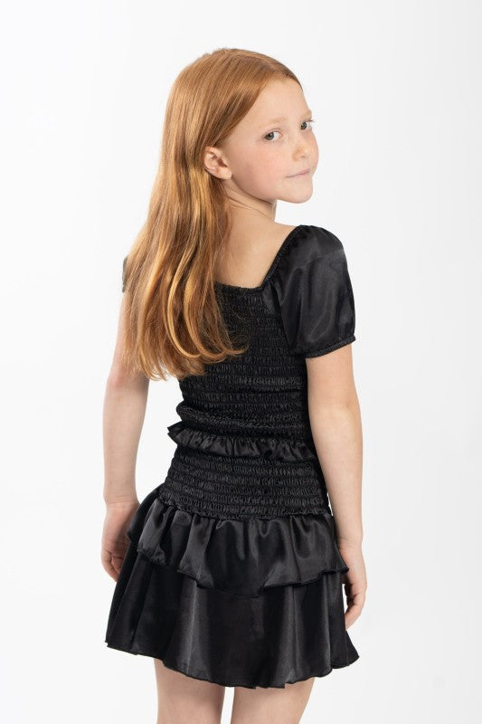 Young girl wearing a black dress with smocked bodice and layered skirt on a white background