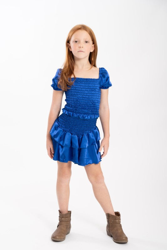 Young girl wearing a blue dress with ruffled details on a white background