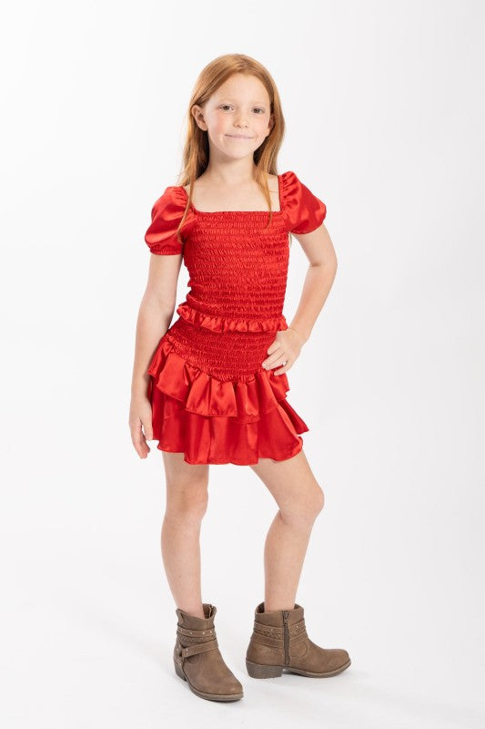Young girl wearing a red dress with puffed sleeves and ruffled details on a white background