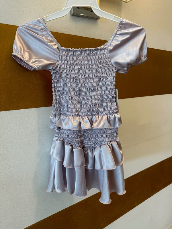 Silver dress with smocked bodice and ruffled skirt on a hanger against a striped background