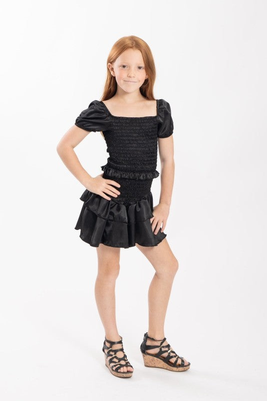 Young girl wearing a black dress with puffed sleeves and ruffled skirt on a white background