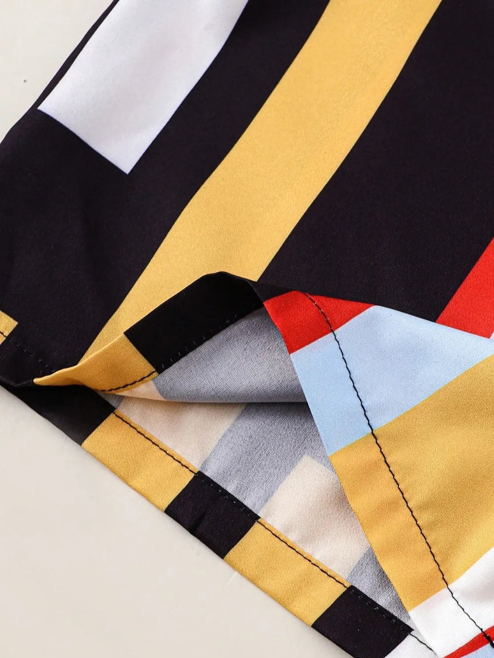 Close-up of the hem of a colorful striped fabric with black, yellow, red, blue, and beige patterns.