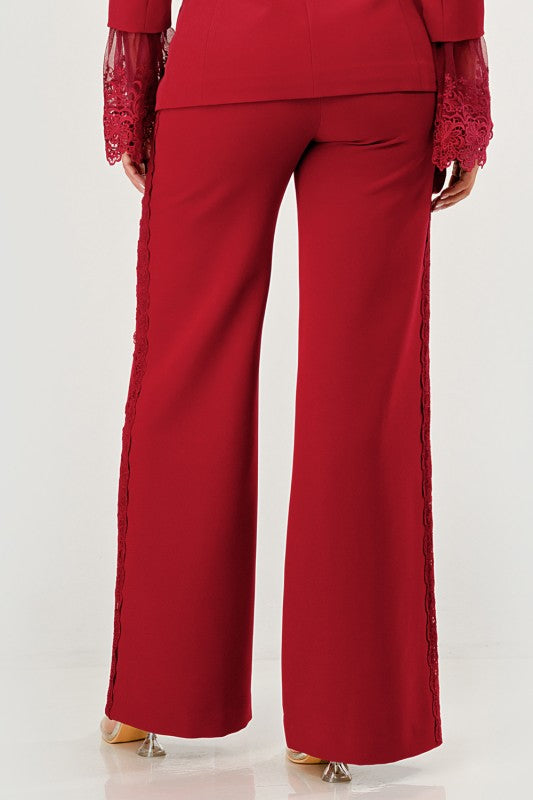 A woman in a red pantsuit. This bold suit features a deep V-neck blazer with lace accents on the sleeves and sides of the pants.