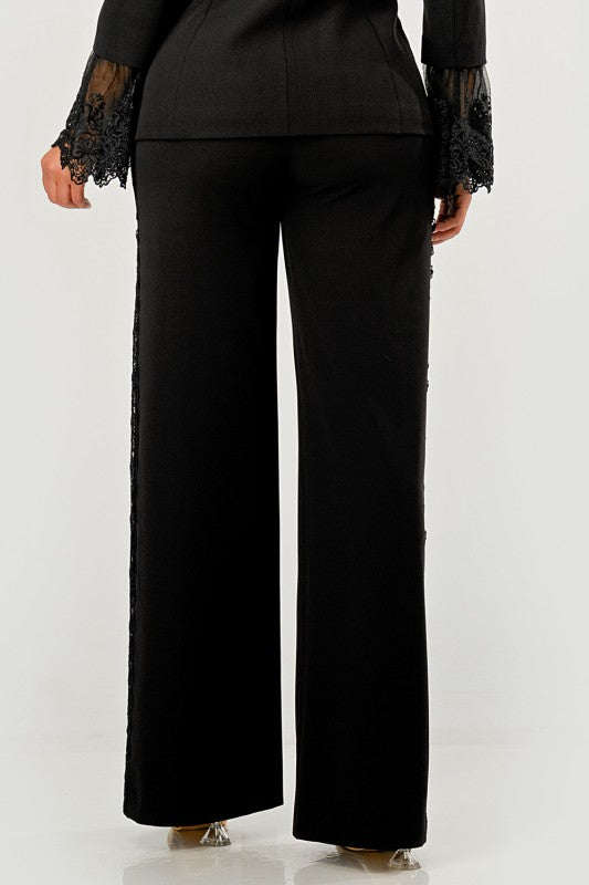 A woman in a black pantsuit. This bold suit features a deep V-neck blazer with lace accents on the sleeves and sides of the pants.