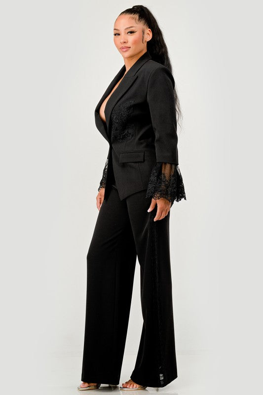 A woman in a black pantsuit. This bold suit features a deep V-neck blazer with lace accents on the sleeves and sides of the pants.