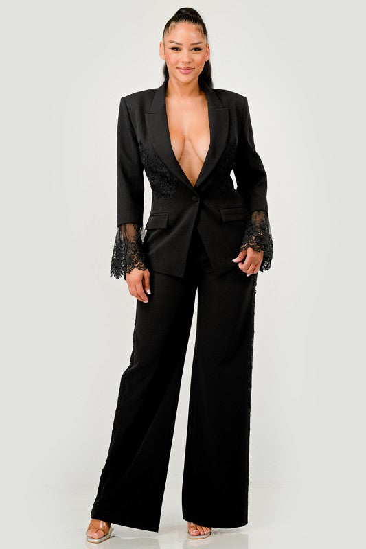 A woman in a black pantsuit. This bold suit features a deep V-neck blazer with lace accents on the sleeves and sides of the pants.