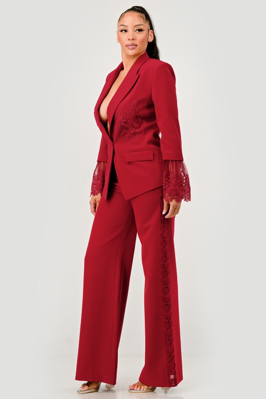 A woman in a red pantsuit. This bold suit features a deep V-neck blazer with lace accents on the sleeves and sides of the pants.