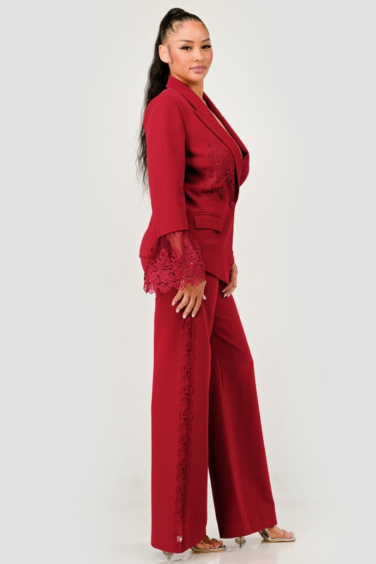 A woman in a red pantsuit. This bold suit features a deep V-neck blazer with lace accents on the sleeves and sides of the pants.