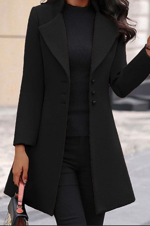 A woman rocking a sleek black outfit. She's wearing a long black coat with buttons down the front, a black top underneath, and matching black pants.