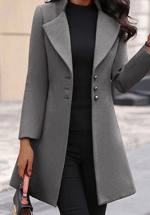 A woman wearing a long gray coat with big lapels and buttons down the front, paired with a black top and pants.