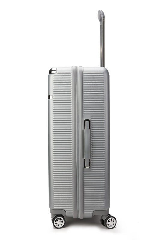 Silver hard-shell suitcase with vertical ribbed texture, extended telescopic handle, and four spinner wheels—positioned upright on a wooden floor.