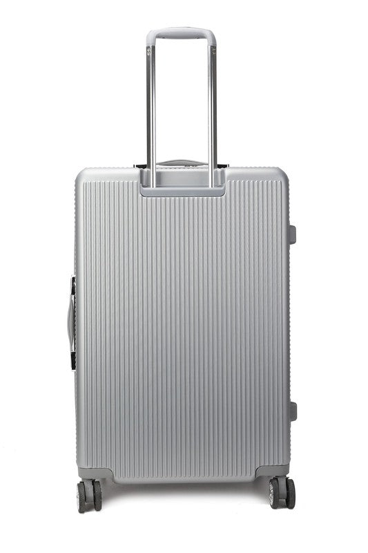Silver hard-shell suitcase with vertical ribbed texture, extended telescopic handle, and four spinner wheels—positioned upright on a wooden floor.