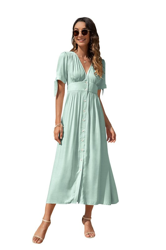 A woman in a cream-colored maxi dress with short sleeves and a V-neckline, wearing sunglasses and strappy heels, standing against a white background.