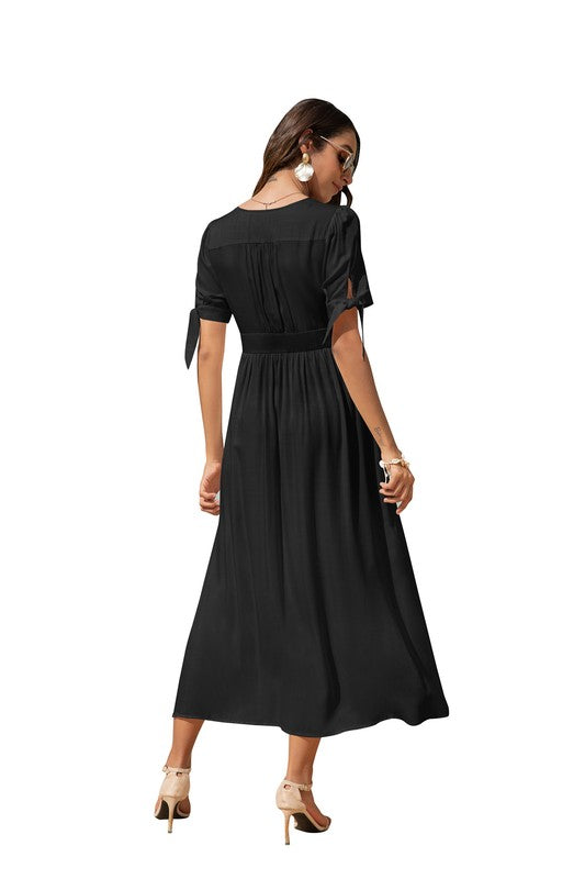 A woman in a black maxi dress with short sleeves and a V-neckline, wearing sunglasses and strappy heels, standing against a white background.