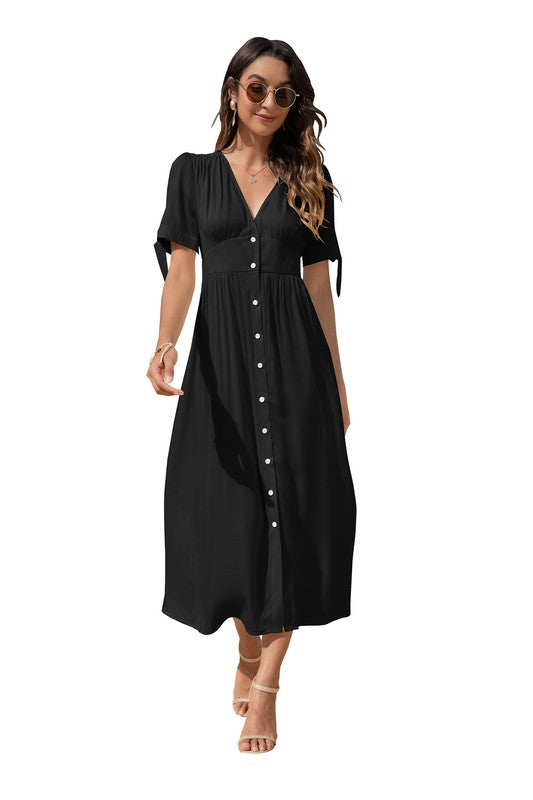 A woman in a black maxi dress with short sleeves and a V-neckline, wearing sunglasses and strappy heels, standing against a white background.