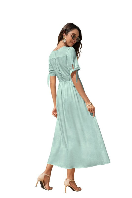 A woman in a cream-colored maxi dress with short sleeves and a V-neckline, wearing sunglasses and strappy heels, standing against a white background.
