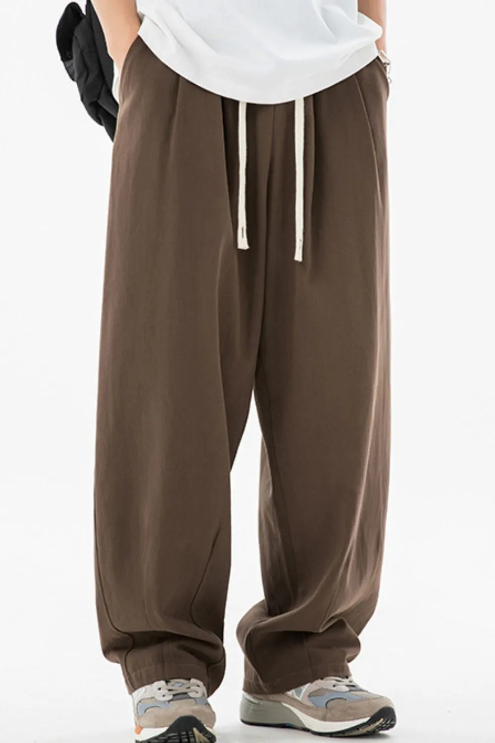 Brown wide-leg pants with a white shirt and gray sneakers on a white background