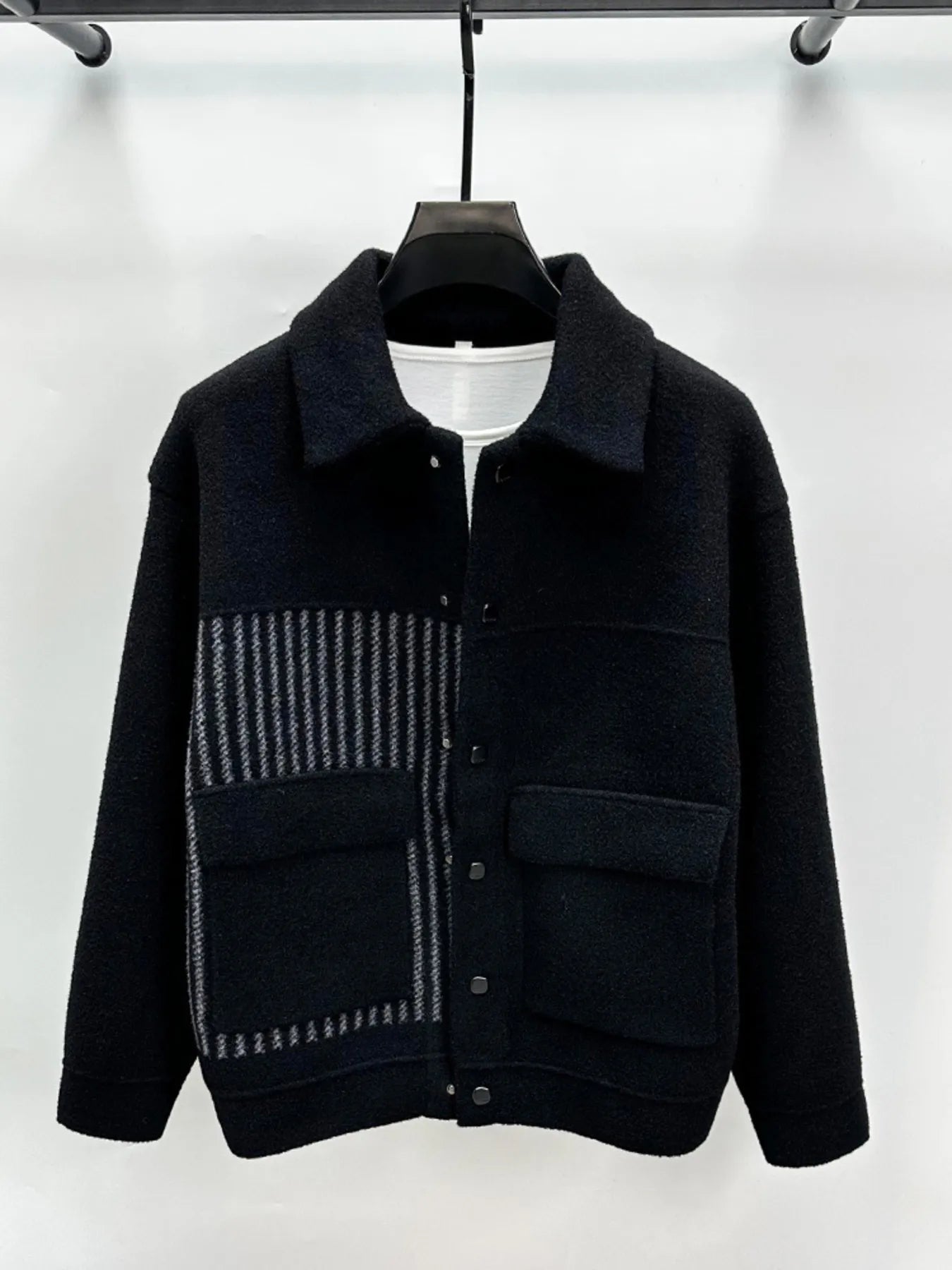 Black jacket with patterned patch on a hanger against a white background