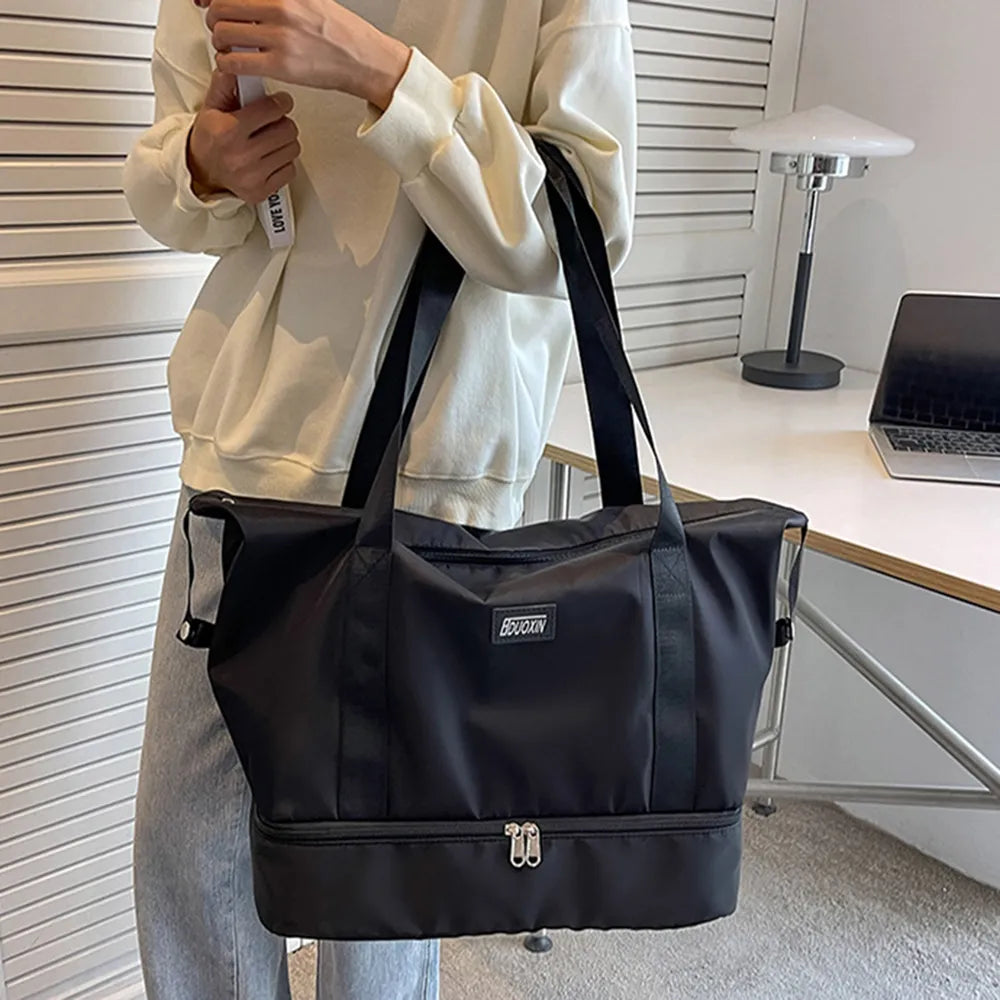 A lady holding a black tote bag with black handles and dual zippered compartments, set against a soft indoor background. Chic and practical—ideal for gym, travel, or daily use.