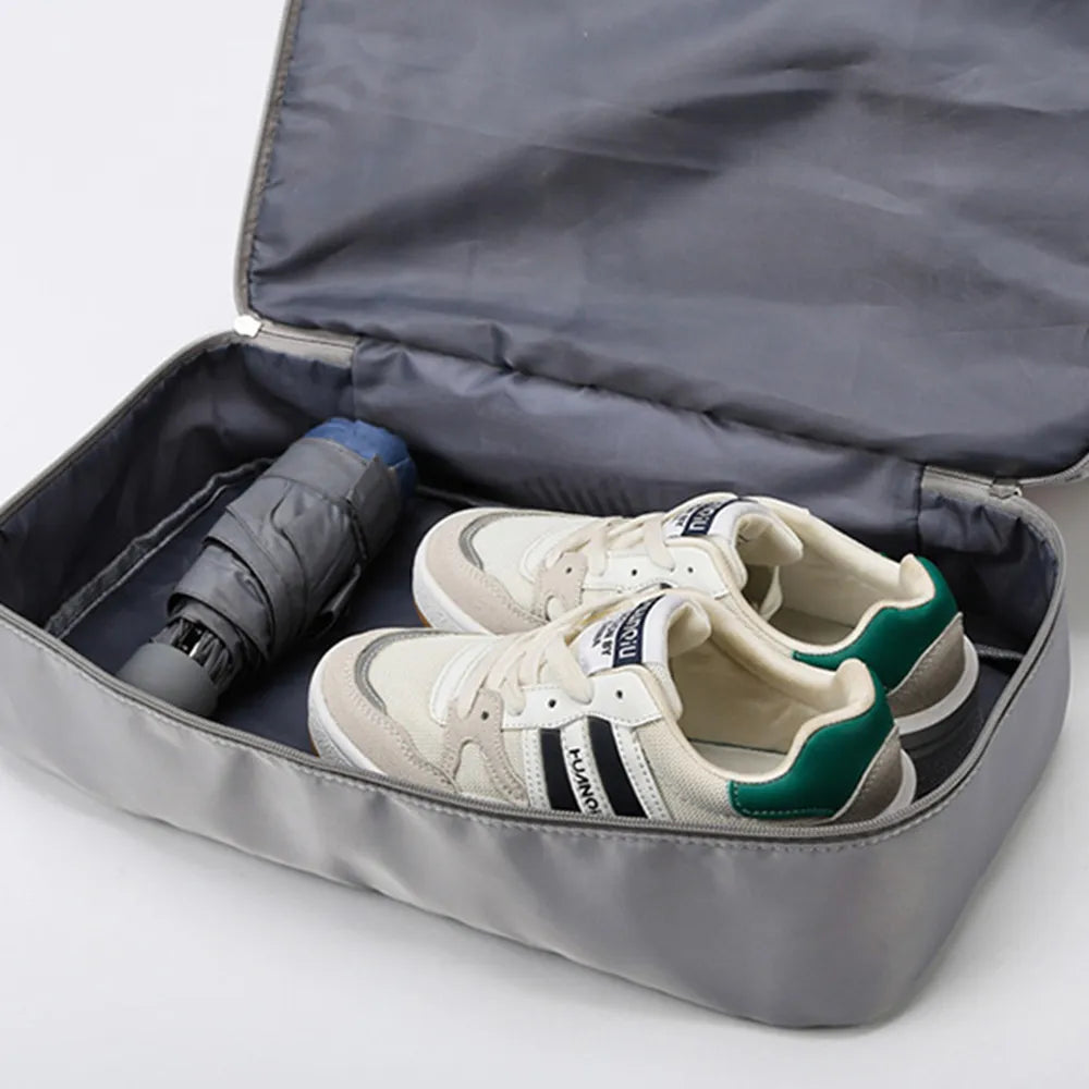Open gray travel bag containing white sneakers with green accents and a folded dark gray umbrella. Neatly packed—ideal for organized travel.