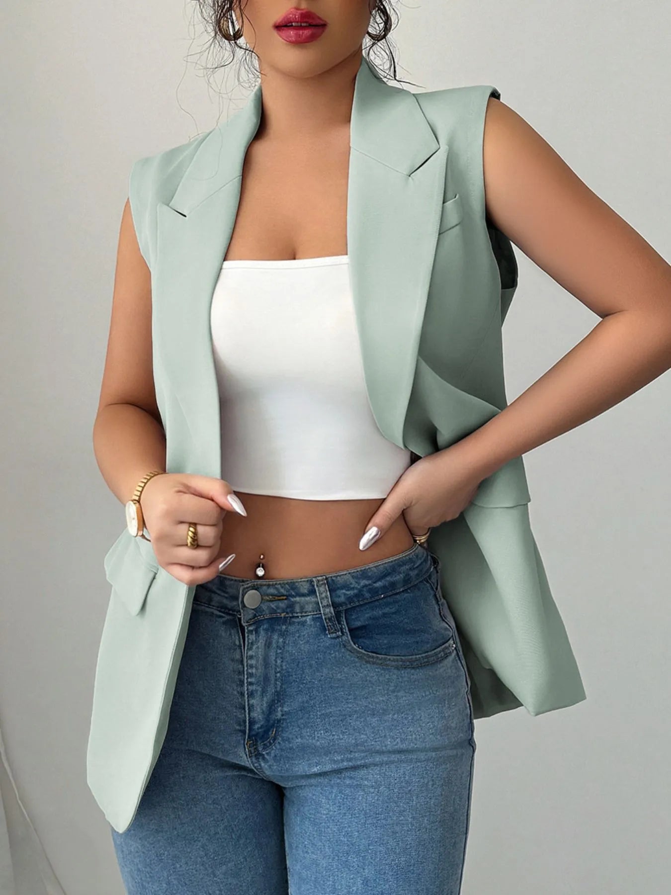 A woman wearing a mint green sleeveless blazer with a white top underneath, paired with blue jeans.