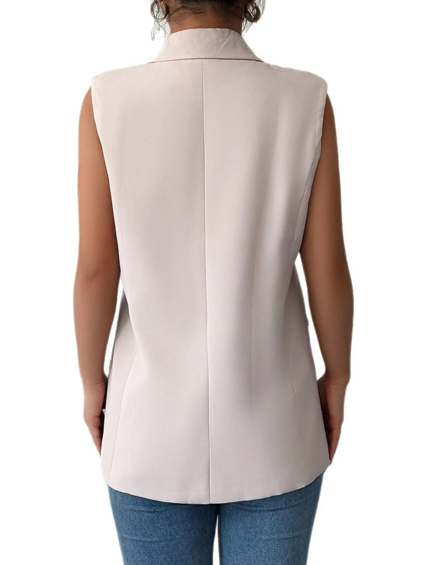 The lady is rocking a sleeveless light pink blazer vest over a white top with blue jeans.