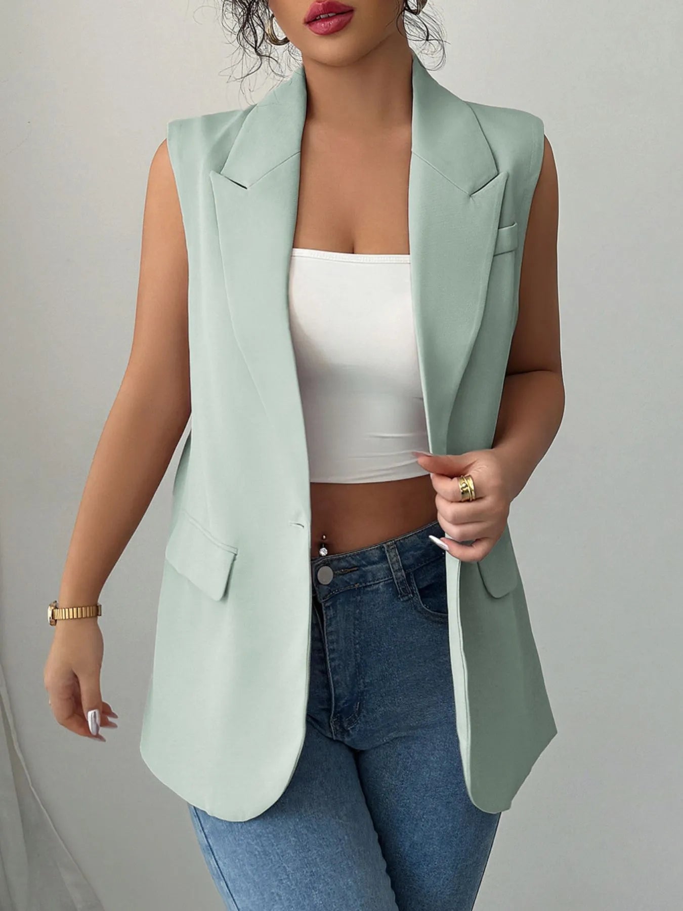 A woman wearing a mint green sleeveless blazer with a white top underneath, paired with blue jeans.