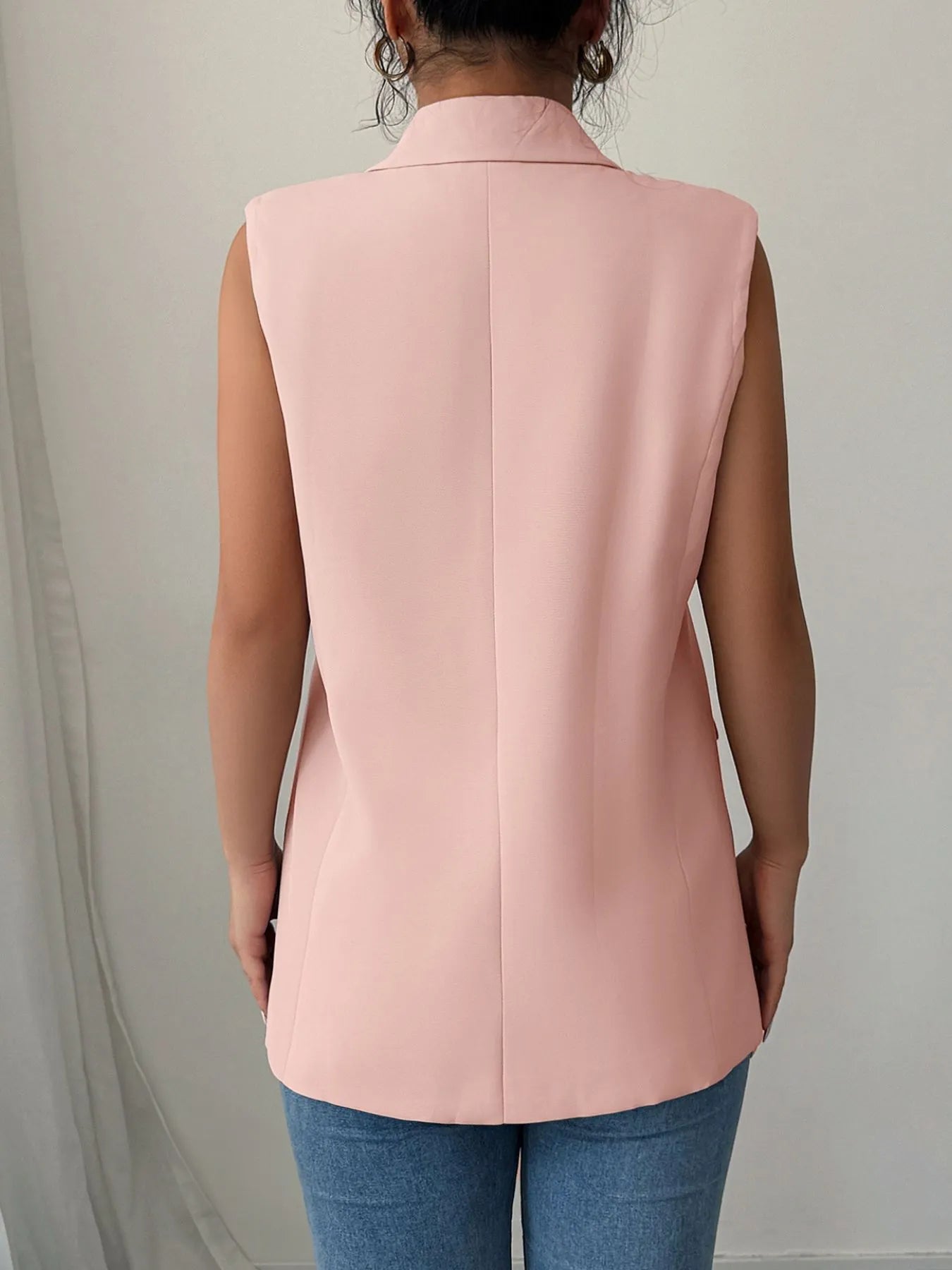 A woman wearing a pink sleeveless blazer with a white top underneath, paired with blue jeans.