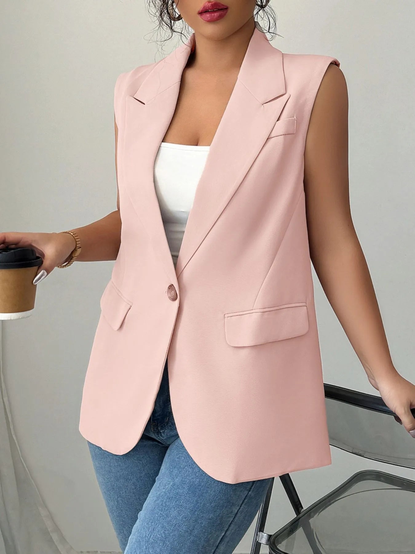 A woman wearing a pink sleeveless blazer with a white top underneath, paired with blue jeans.
