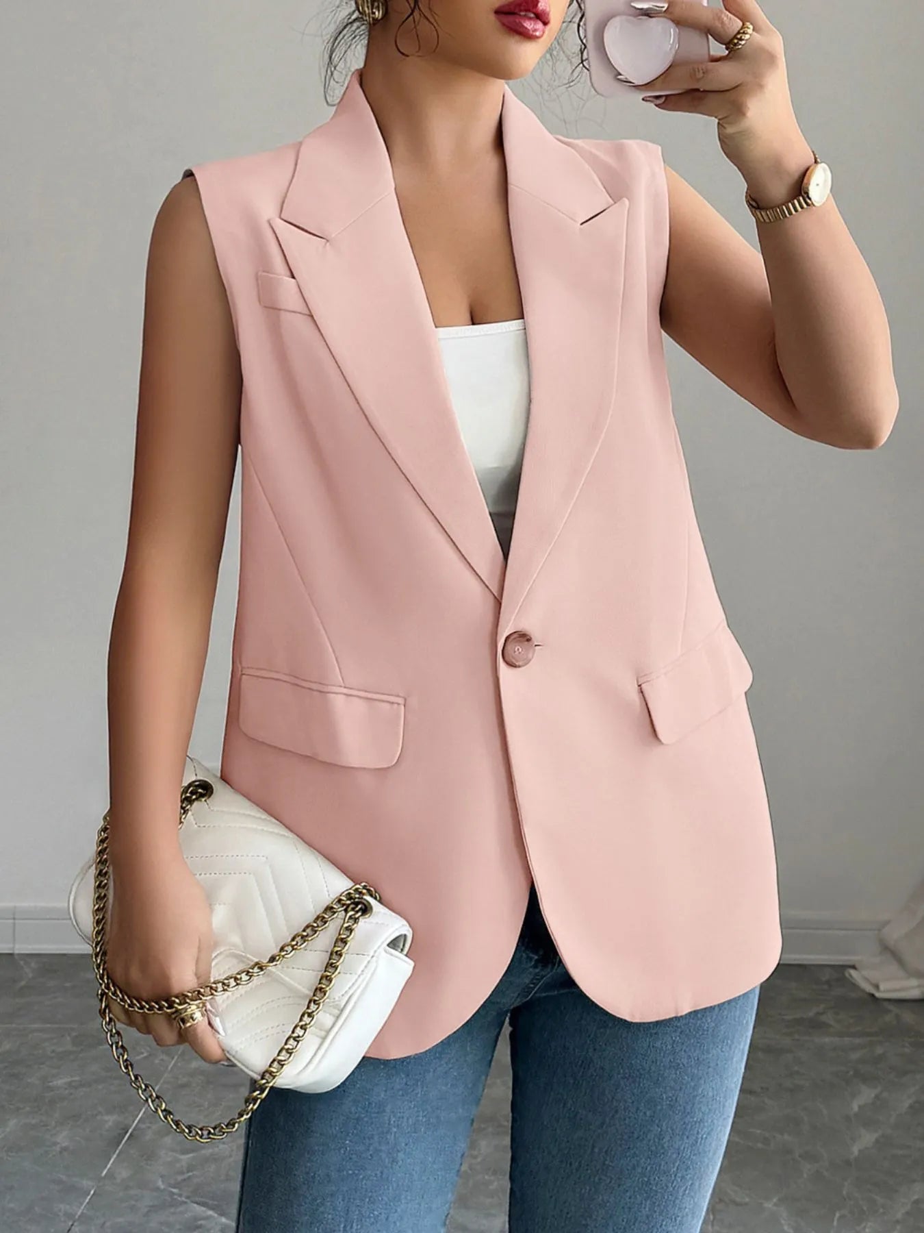 A woman wearing a pink sleeveless blazer with a white top underneath, paired with blue jeans.