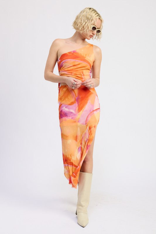 A model wearing a vibrant one-shoulder maxi dress with an abstract orange, pink, and yellow print.