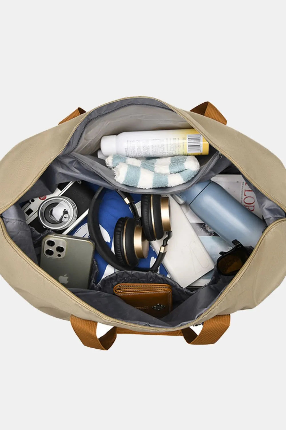 Open beige travel bag with brown handles, showcasing neatly packed essentials: headphones, iPhone, wallet, sunglasses, socks, water bottle, and more. Stylish and spacious—perfect for organized travel or gym use.