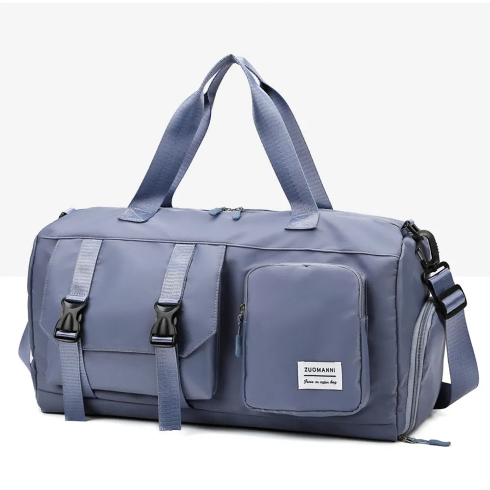 Muted blue duffel bag with short handles and an adjustable shoulder strap, featuring a flap pocket with black buckles and a zippered front pocket.  Durable and stylish—ideal for gym or travel.