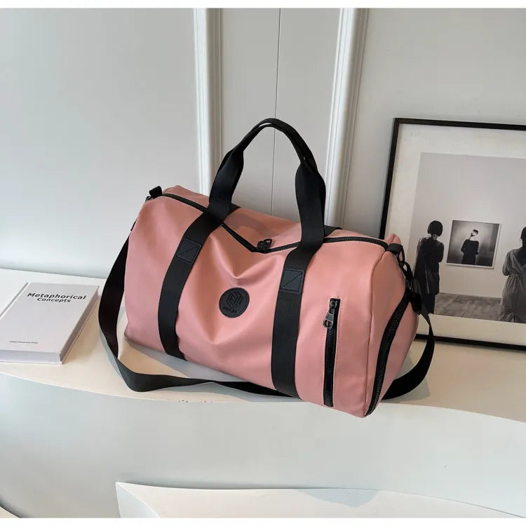 Pink duffel bag with black straps and a circular logo, placed on a dark wooden surface. Stylish and motivational setup—great for travel or gym use.