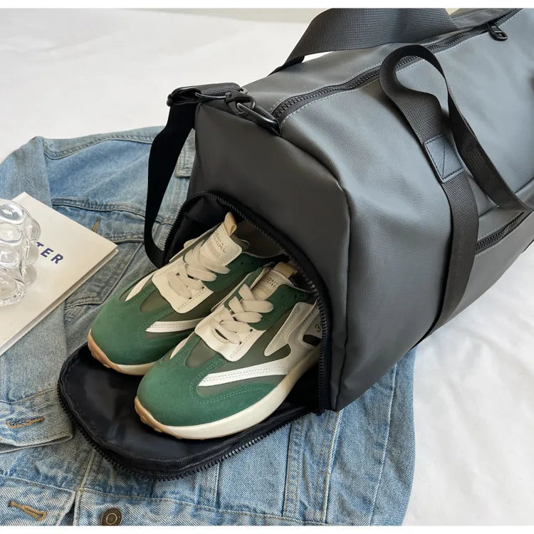 Gray duffel bag with a dedicated shoe compartment holding green and white athletic shoes, placed on a blue denim jacket. Practical and organized—perfect for gym or travel use.