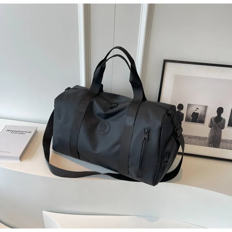 Gray duffel bag with black straps and a circular "BUBM" logo, placed on a white curved surface. Features zippered compartments and padded handles—sleek, minimalist, and ideal for travel or gym use.