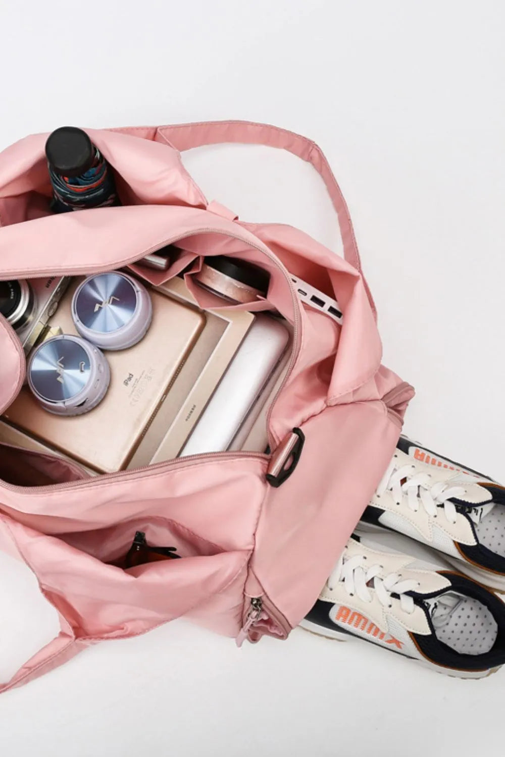 Open pink gym bag neatly packed with white sneakers, pink water bottle, towel, cosmetics, headphones, and a tablet. Stylish and organized—perfect for fitness or travel.