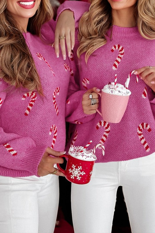 Two women in pink candy cane print sweaters and white pants with festive beverages