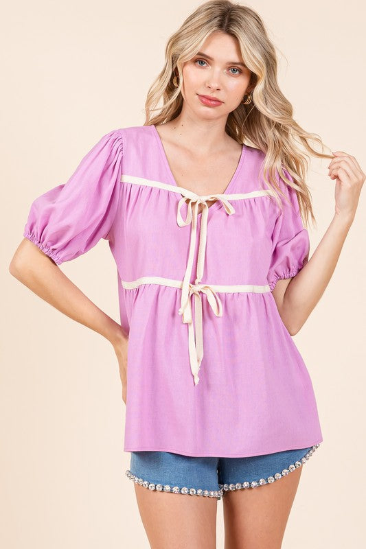With piping along edges and seams, this babydoll top balances softness and structure.