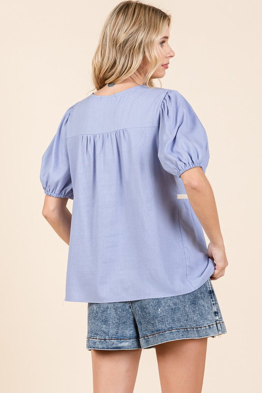 The piped edges contrast beautifully against the flowing body of the blouse.