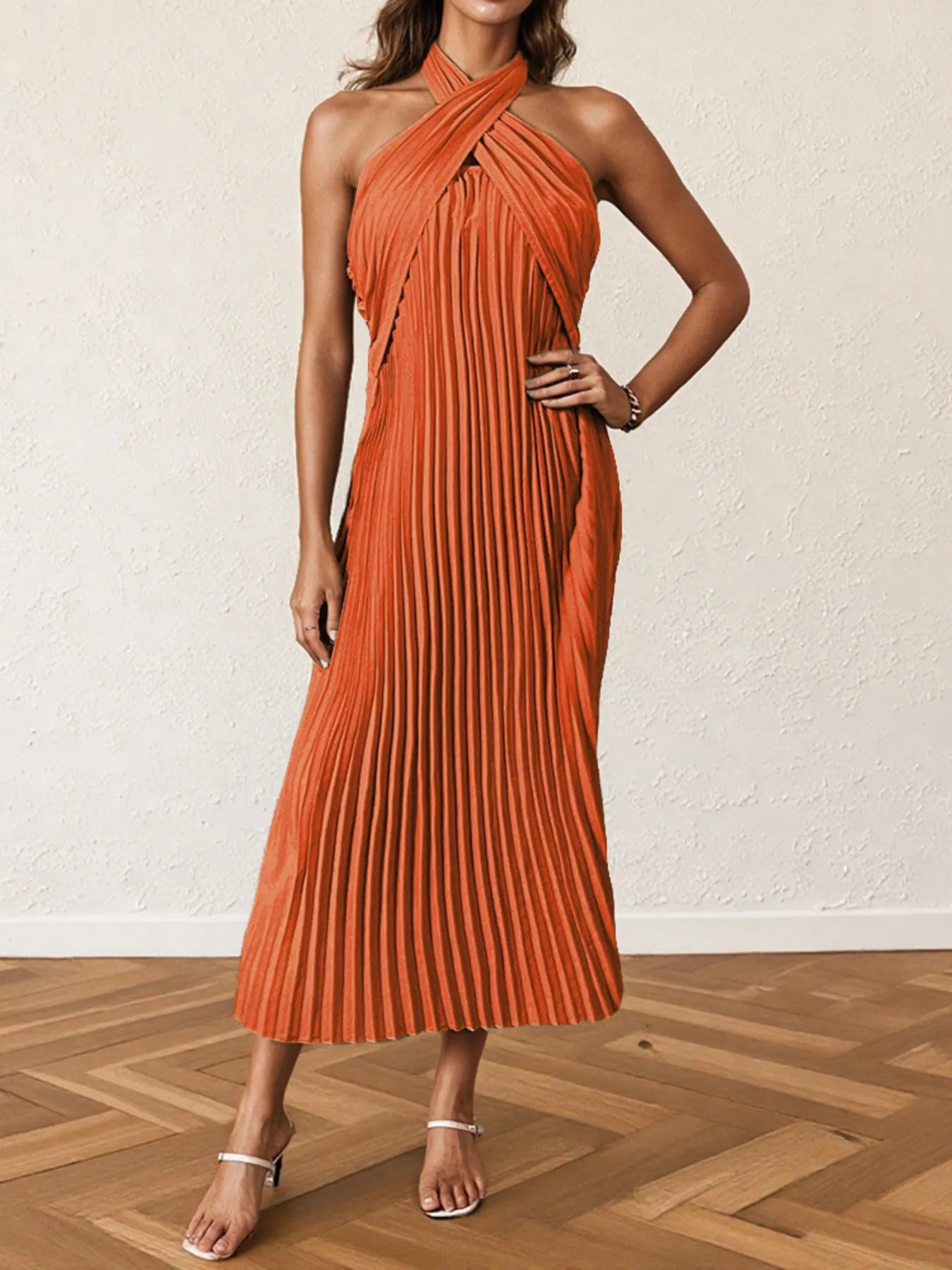 Woman wearing a pleated halter neck midi dress with crisscross neckline..