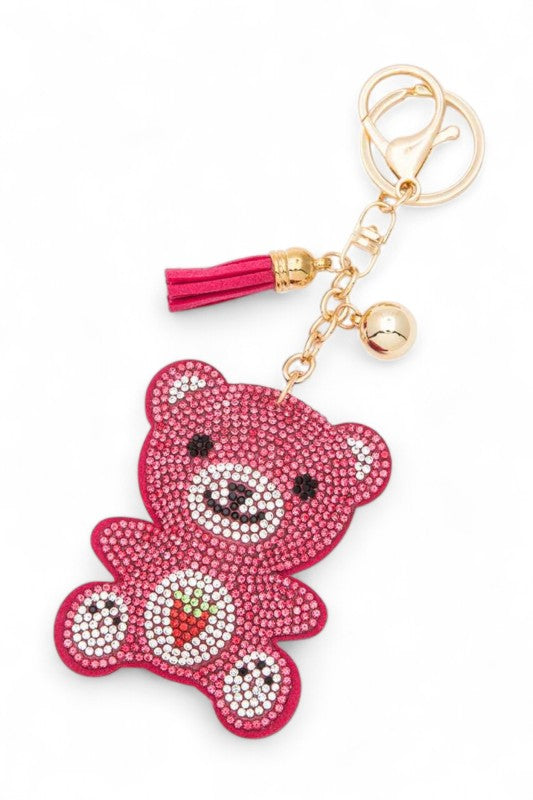 A pink teddy bear made of rhinestones with a strawberry design on its tummy. Got a gold chain with a pink tassel and a gold ball attached to a gold keyring. Looks like a fun accessory.